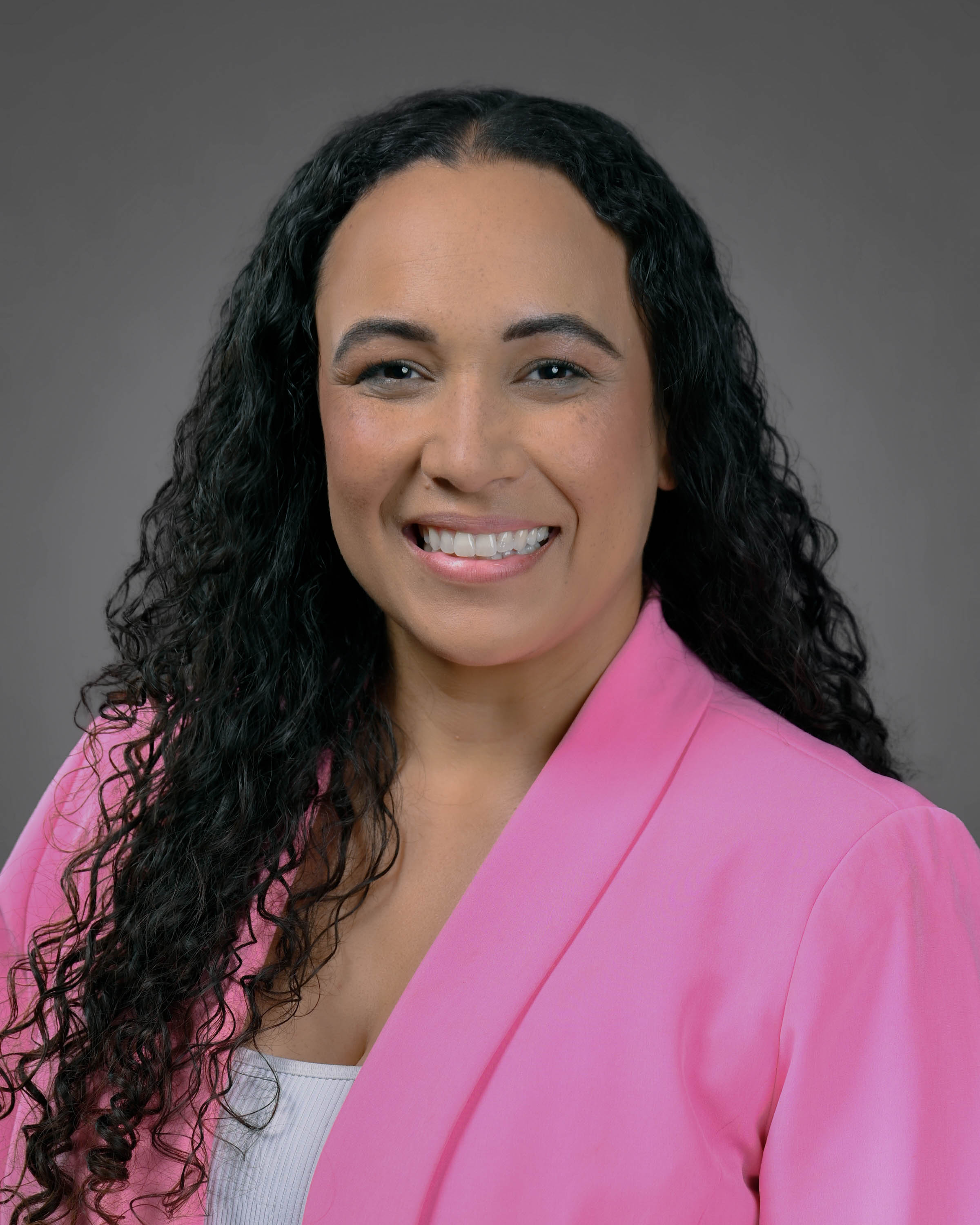 Woman smiling with long dark curly hair and a pink jacket